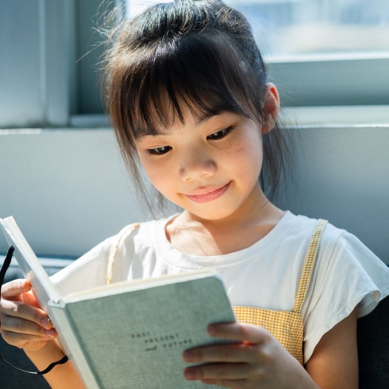 Little girl reads book by window