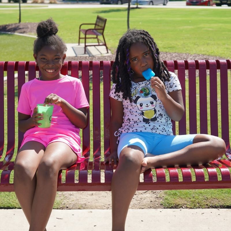 Two girls eat popsicles at popsicles in the park